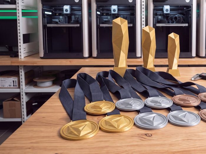 Série 3D tištěných medailí se stuhami a trofeje ve zlatém odstínu